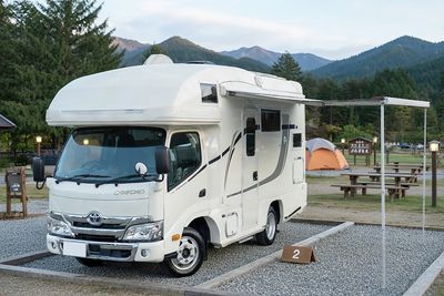 Toyota Camroad motorhome at a Japanese campground with awning, mountains and forest backdrop, premiu