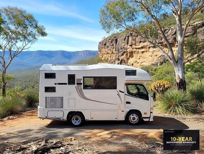 White camper van parked in a scenic mountainous area with blue sky.