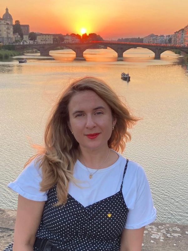 Woman smiling near a river at sunset with a bridge in the background.