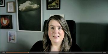 Woman with long hair sitting in a chair, wall art in the background.