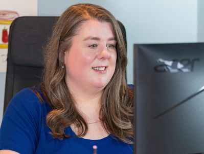 Woman in a blue shirt working on a computer at her desk.