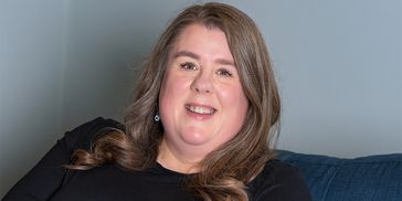 Smiling woman with wavy hair and leopard print skirt relaxing on a blue couch.