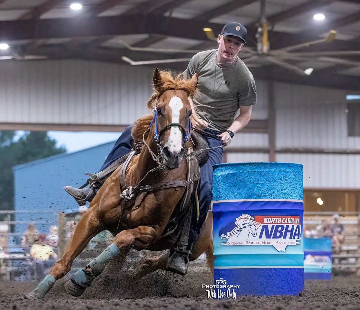 Rider swiftly guiding horse around a barrel in an indoor rodeo arena.