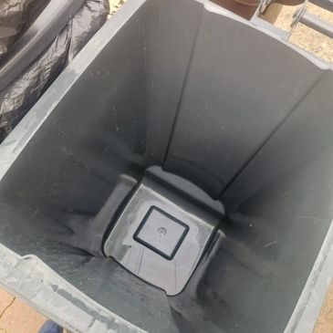 Empty black plastic trash bin outdoors on pavement.