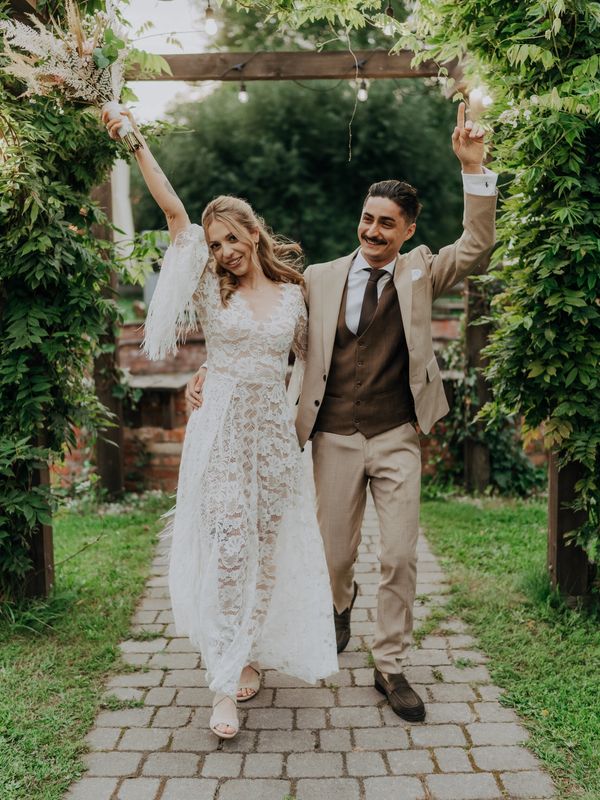 Newlywed couple joyfully celebrating under a garden archway.