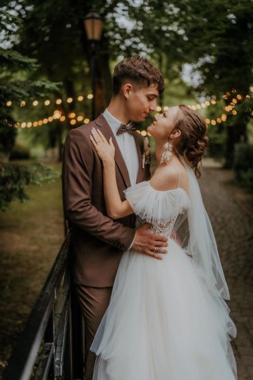 A bride and groom share a romantic moment outdoors with soft string lights.