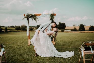 Bride and groom share a romantic dip kiss outdoors at their wedding ceremony.