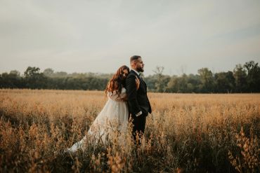 Bride and groom embrace in a golden field at sunset.