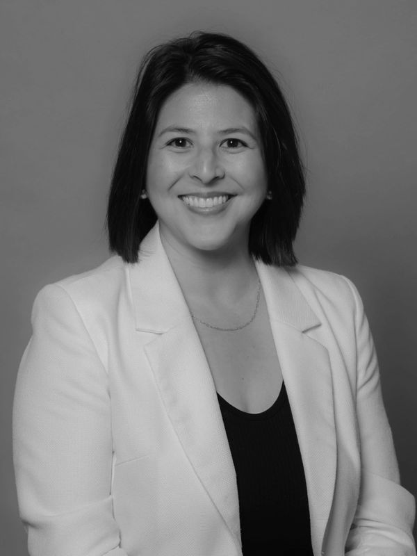 Smiling woman in a white blazer against a plain background.