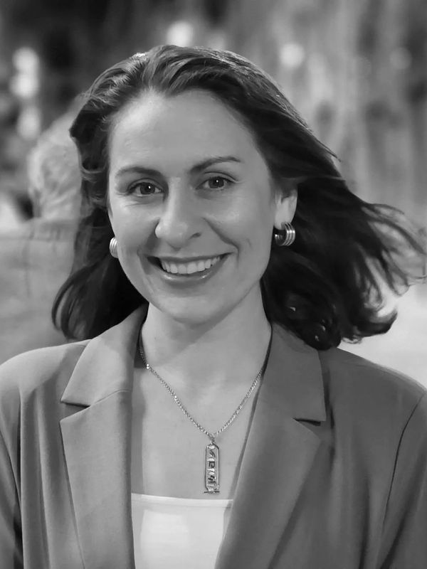 Smiling woman in a blazer with earrings and a necklace.