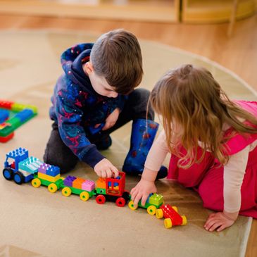 Two young kindy children playing on a mat with a Lego duplo train.