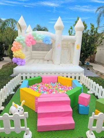 Colorful ball pit and white inflatable castle decorated with balloons in a backyard.