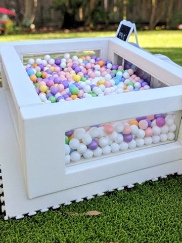 A white ball pit box filled with colorful balls on grass.