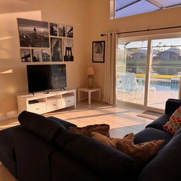 Cozy living room with black couch and pool view through sliding doors.