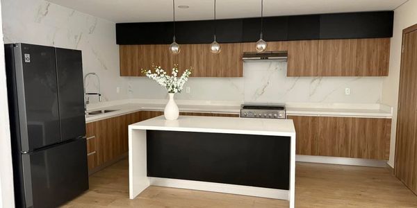 Amplia cocina moderna en color nogal con  isla de quarzo refrigerador grande negro y florero blanco