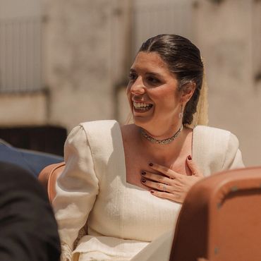 Mujer sonriente con vestido blanco sosteniéndose el pecho.