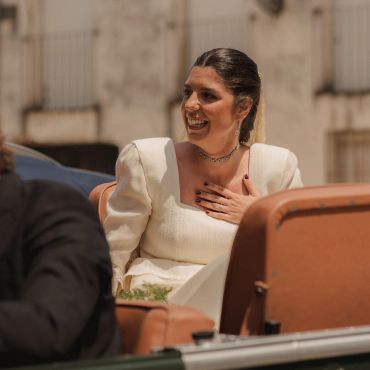 Mujer sonriente con vestido blanco sosteniéndose el pecho.
