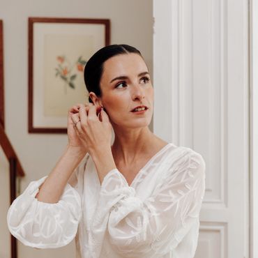Mujer poniéndose un pendiente con vestido blanco.