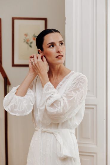 Mujer poniéndose un pendiente con vestido blanco.