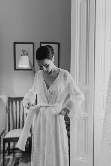 Mujer ajustándose un vestido blanco en una habitación.