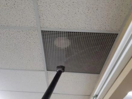 A black pole inserted into a ceiling vent panel in an indoor space.