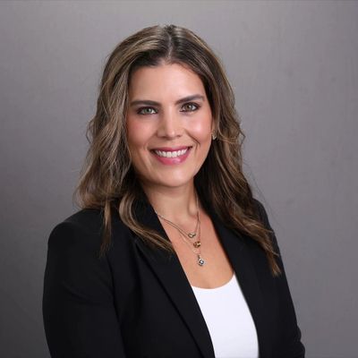 Professional woman smiling confidently in business attire against gray background.