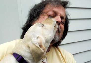 "Unconditional Love" - portrait of golden labrador puppy "kissing" a young man who leans back loving