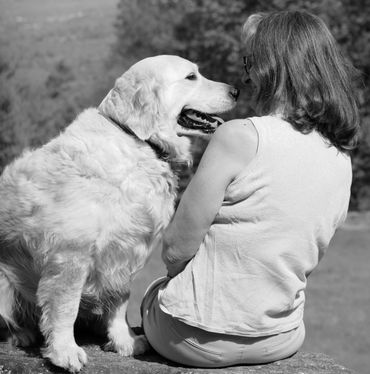 LUNA & HANDLER. Golden Retriever, both seated on rock, dog leans towards handler, she leans back