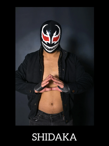Masked wrestler Shidaka poses with hands together, wearing black jacket and gloves.