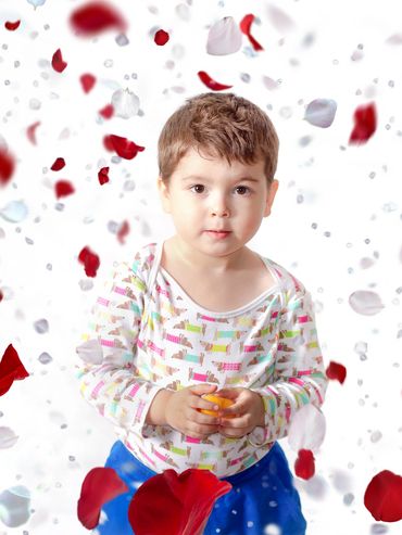 A young child surrounded by falling red and white flower petals.