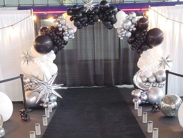 A black carpet runway with a black, white, and silver balloon arch and star decorations.