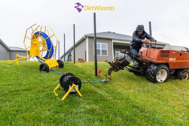 Man operating a machine on a grassy hill with equipment in the background.