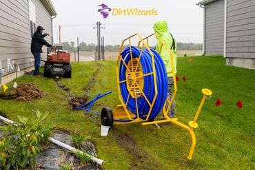 Technician using blue tubing reel for underground pipe installation between houses.