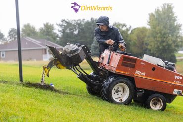 Operator using a ditch witch machine for trenching in a grassy area.