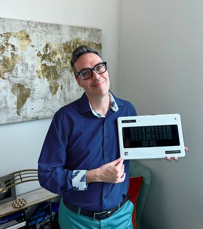 Thomas holding his steno machine, dressed in business casual clothes and wearwearing glasses.