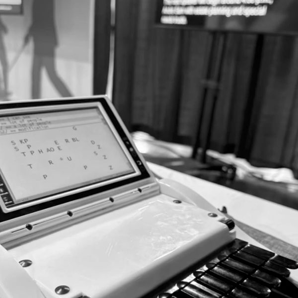Black and white photo of a steno machine's screen and the background of an Abilities Expo workshop s