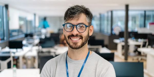 Smiling man with glasses and beard in a modern office space.