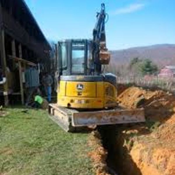 Yellow excavator digging a trench beside a building on a sunny day.