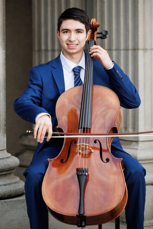 Young man in blue suit playing cello with a smile.