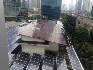 Worker on rooftop with solar panels in urban area.