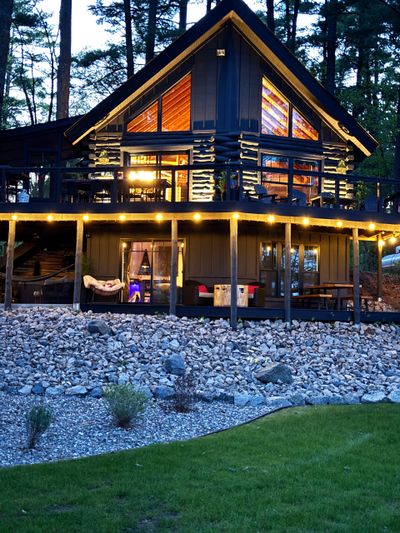 Cozy illuminated cabin with large windows in a forest setting at dusk.
