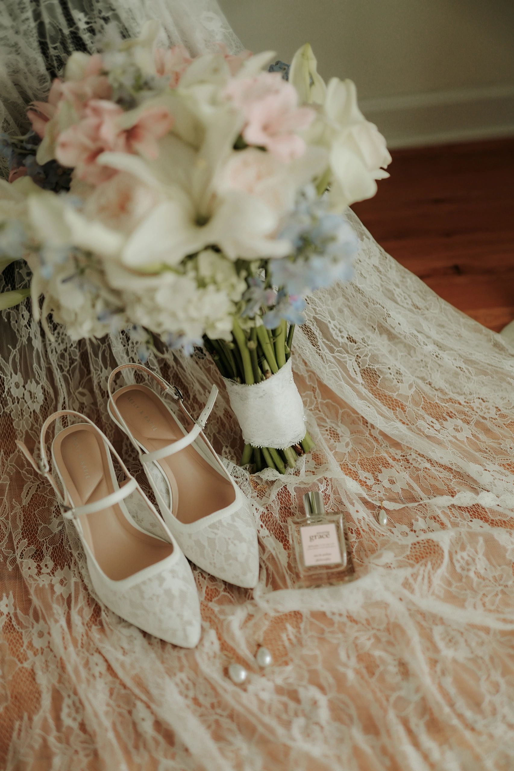 Wedding accessories including bouquet, shoes, and perfume on lace fabric.