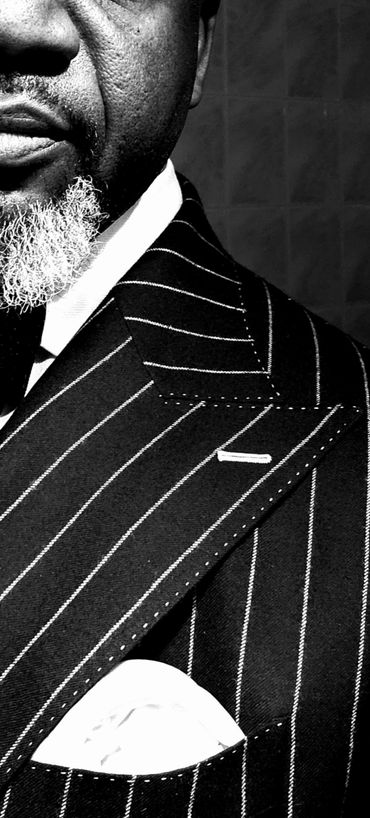 Wide pinstripes, contrasting white pickstitching, and sharp peak lapels create bold bespoke elegance