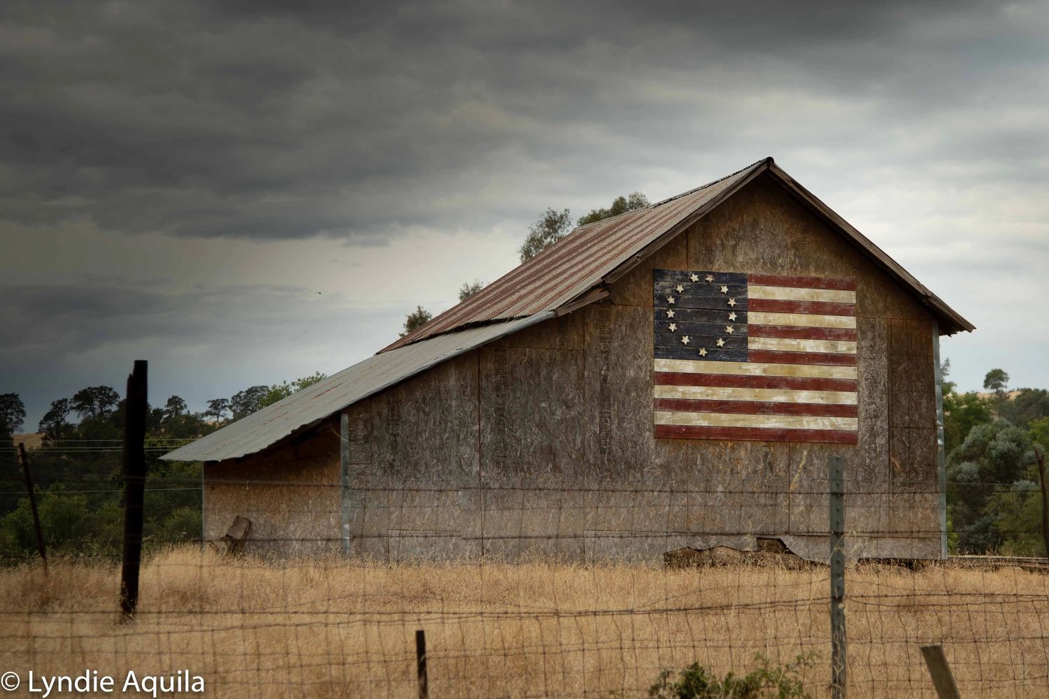 A rustic barn with a historic Betsy Ross American flag under a cloudy sky.