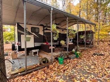 Covered patio with hanging plants beside an RV in autumn.