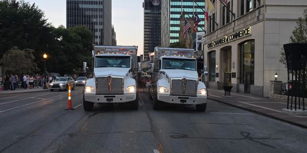 Two large white trucks parked side by side on a city street.