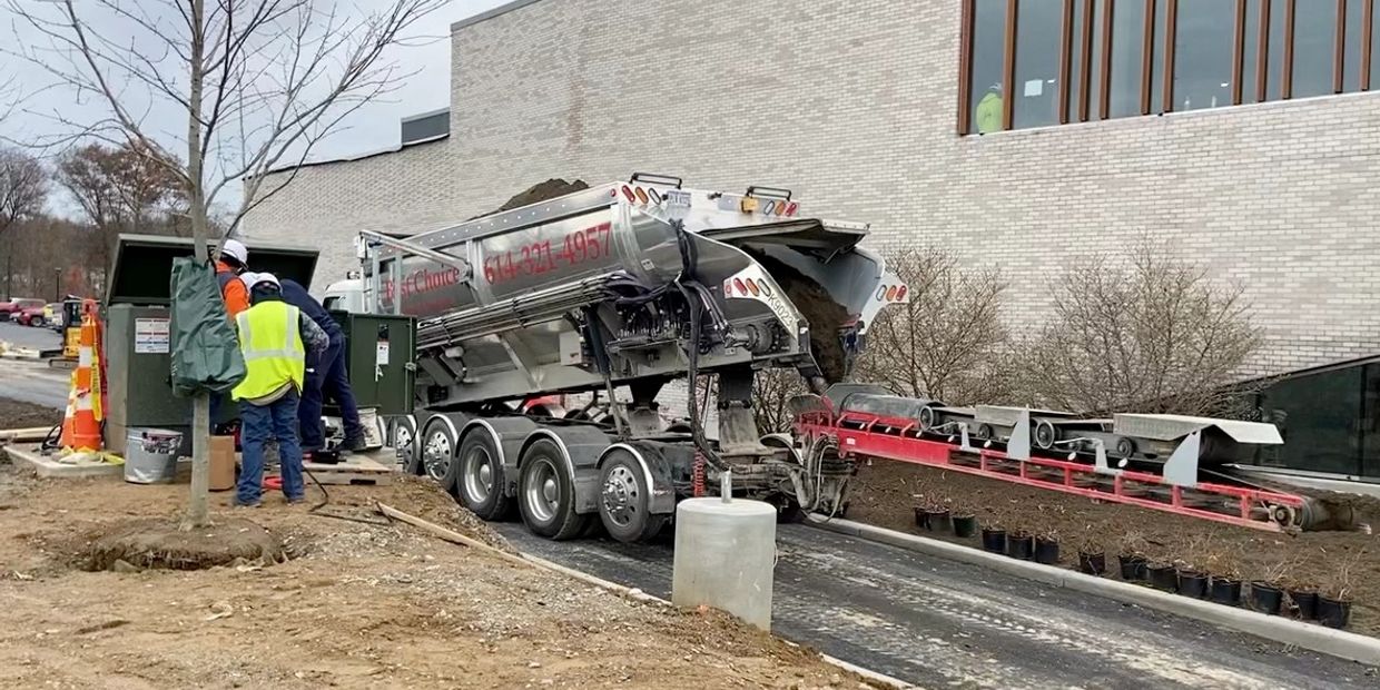 Workers operate machinery unloading soil at a construction site near a building.