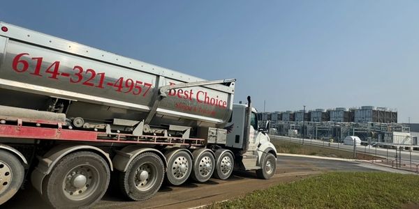 A large tanker truck parked near an industrial facility under clear skies.