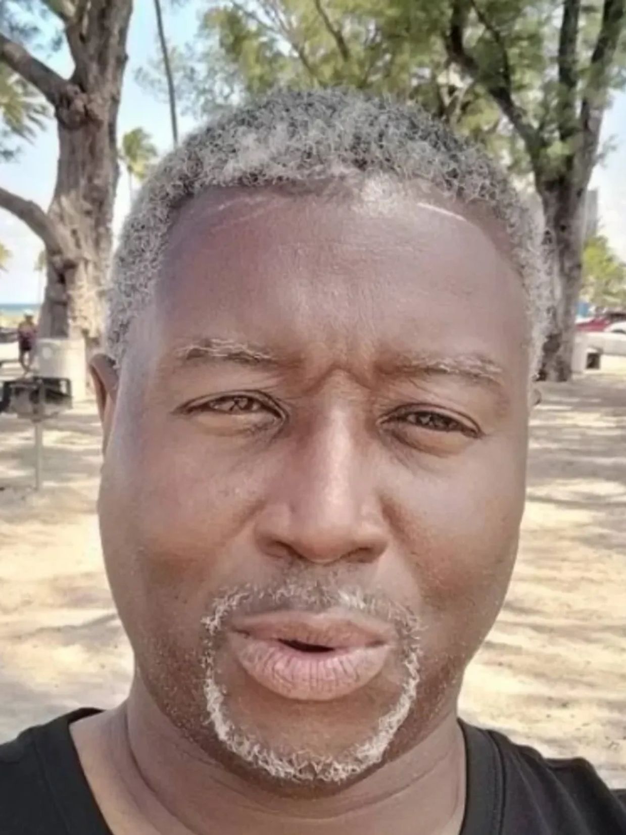 Close-up of a man with gray hair and beard outdoors.