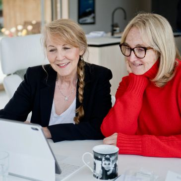 Two mature women smiling while looking at a tablet together.